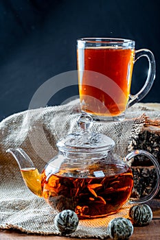Tea in a glass teapot with a blooming large flower. Teapot with exotic green tea-balls blooms flower and a glass Cup of tea. Tea