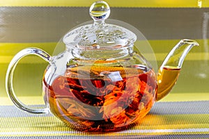 Tea in a glass teapot with a blooming large flower. Teapot with exotic green tea-balls blooms flower. Tea ceremony on green