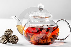 Tea in a glass teapot with a blooming large flower. Teapot with exotic green tea on a white background with dried balls-buds for