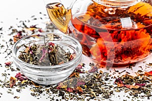 Tea in a glass teapot with a blooming large flower. Teapot with exotic green tea on a white background with scattered dried tea