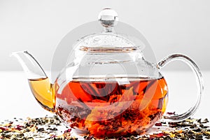 Tea in a glass teapot with a blooming large flower. Teapot with exotic green tea on a white background with scattered dried tea