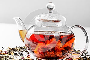 Tea in a glass teapot with a blooming large flower. Teapot with exotic green tea on a white background with scattered dried tea