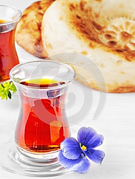 Tea in glasses of armudu, next to two freshly baked cake - tandoor bread, white wooden background. Close-up, breakfast or lunch