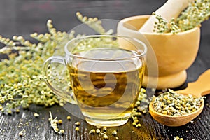 Tea of gray wormwood in glass cup with mortar on dark board