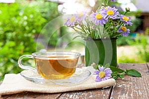 Tea herbal useful for health on on canvas, on a wooden table, next to the lilac flowers in a metal mug