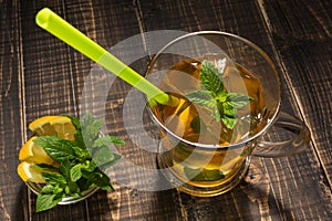 Tea with ice and mint in a glass cup on wooden boards, near mint and lemon, a refreshing drink