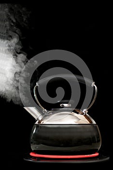 Tea kettle with boiling water on black background