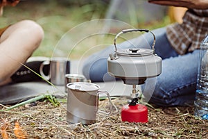 A tea kettle on a propane stove next to a metal cup