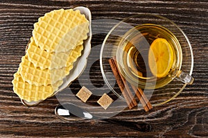 Tea with lemon in cup, cinnamon on saucer, wafers in plate, sugar, teaspoon on table. Top view