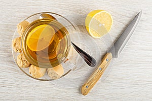 Tea with lemon in cup, creamy fudge, spoon on saucer, piece of lemon, knife on wooden table. Top view