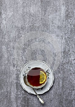 Tea with lemon in teacup with saucer and spoon at gray background