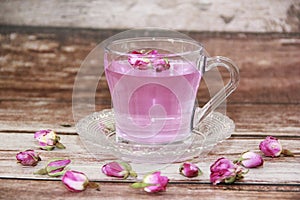 Tea made from pink rose petals in a transparent glass mug and small flower buds on a wooden background