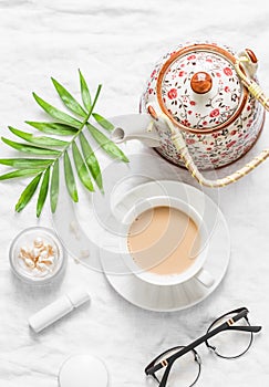 Tea with milk. Masala tea, teapot, cosmetics, lipstick, facial oil, glasses, green leaf flower on light background, top view. Cozy