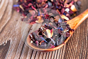 Tea mix of karkade, flowers and berries in a spoon and on the table