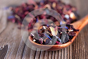 Tea mix of karkade, flowers and berries in a spoon and on the table