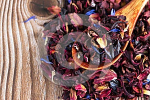 Tea mix of karkade, flowers and berries in a spoon and on the table