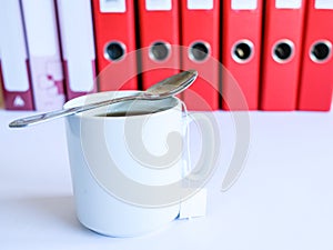 Tea at the office. White ceramic mug with tea on the background of red office folders for documents