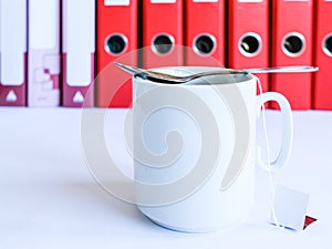 Tea at the office. White ceramic mug with tea on the background of red office folders for documents