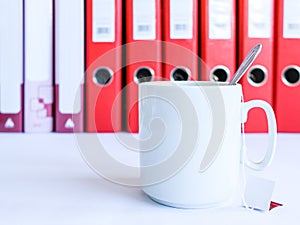 Tea at the office. White ceramic mug with tea on the background of red office folders for documents