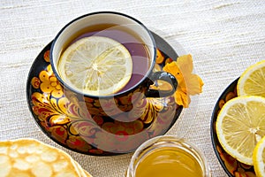 Tea in a painted Cup, on a saucer sliced lemon, pancakes, sour cream and a wooden spoon for overlaying. tea party in rustic style