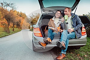 Tea party in car trunk - loving couple drinks hot tea from thermos flask sitting in car trunk