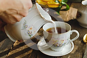 Tea party in rustic style. Pouring milk into tea cup.