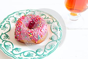 Tea and pink sugar donut on white wooden table