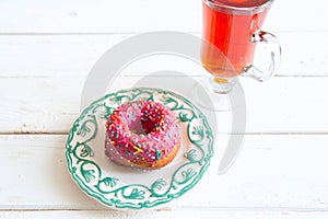 Tea and pink sugar donut on white wooden table