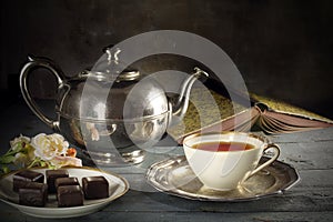 Tea in a porcelain cup, old fashioned silver teapot, chocolate c