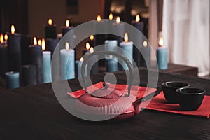 Tea pot with two cups on a wooden table with many candles burning on a background