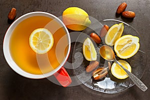 Tea in a red mug. Slices of juicy lemon, dates and spoon of hone