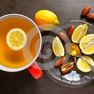 Tea in a red mug. Slices of juicy lemon, dates and spoon of hone