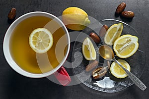 Tea in a red mug. Slices of juicy lemon, dates and spoon of hone