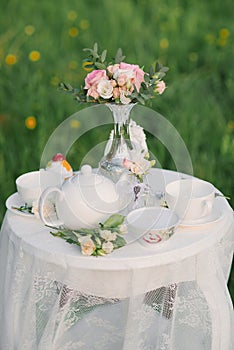 A tea service, a delicate bouquet of roses and eustoma in a silver vase on a coffee table with a lace tablecloth. Wedding decor