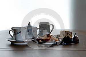 Tea Service & Fruit cake on a wooden table with the scene being backlit with natural light . The images a casual look with coins b