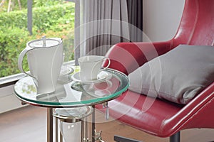 Tea set on glass top table with red easy chair in living room interior