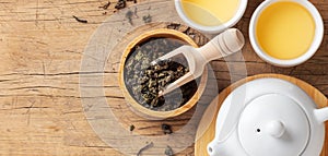 Tea set with teapot and dried tea leaves in bowl on wooden table background, top view