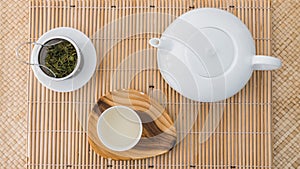 Tea set top view. Porcelain teapot, teacup and green tea in a metal filter on a bamboo tray