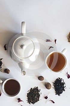 Tea set with white ceramic tea pot, dried rose flowers and other tea ingredients on the white. Flat lay view of various dried teas
