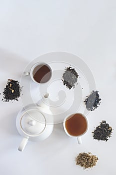 Tea set with white ceramic tea pot and other tea ingredients on the white. Flat lay view of various dried teas and teapot. View
