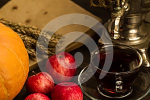 Tea still life with samovar, apples, ripe orange pumpkins, maple leaves, wheat on wooden background.