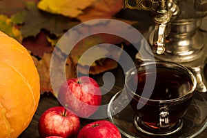 Tea still life with samovar, apples, ripe orange pumpkins, maple leaves on wooden background.