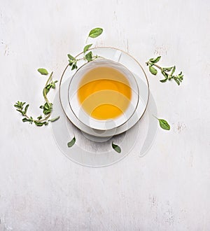 Tea with thyme in a white cup on a white saucer place for text on wooden rustic background top view