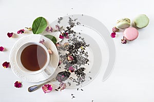 Tea time concept. Beautiful white cup of tea, rose buds, dry tea, green leaves and french macaroons on the white background.