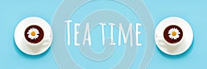 Tea time text and two white cup of tea with chamomile on dish saucer, blue background. Top view Flat lay Banner