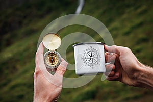 Tea in a tourist metal mug and a compass in Hand Natural background .Vintage Tone