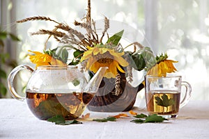 Tea in a transparent teapot and sunflowers in a ceramic vase