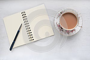 Tea in a vintage cup and saucer, and notebook with blank pages.