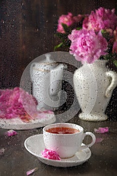 tea in a white porcelain cup on a black table with a bouquet of peonies. Hot drink on a dark background. Concept