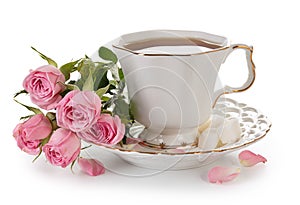 Tea in a white porcelain cup and a bouquet of roses isolated on a white background